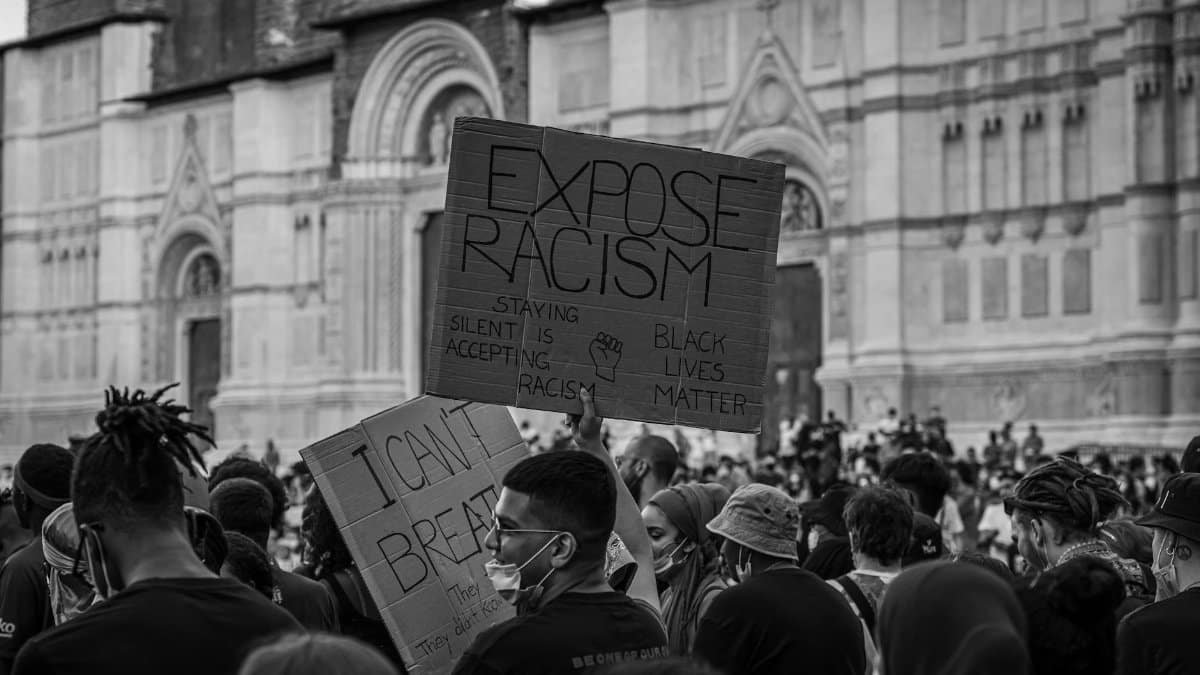 Crowd at a rally holding placards advocating against racism.