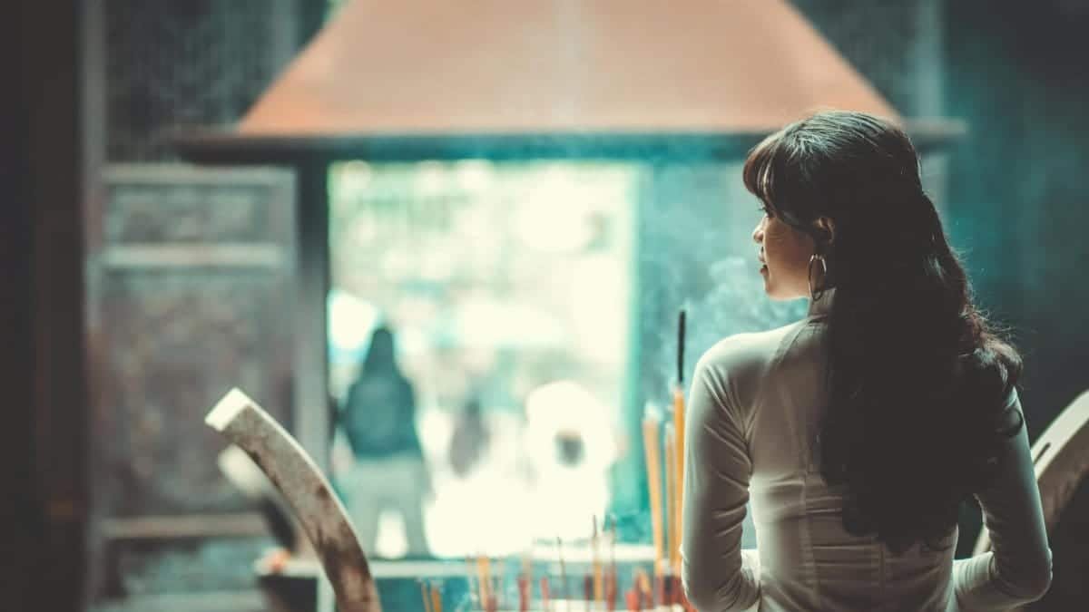A serene scene of a woman in an Ao Dai by incense in a Vietnamese temple.