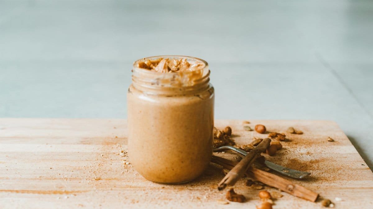 Creamy homemade peanut butter in a jar with cinnamon sticks on a wooden board.