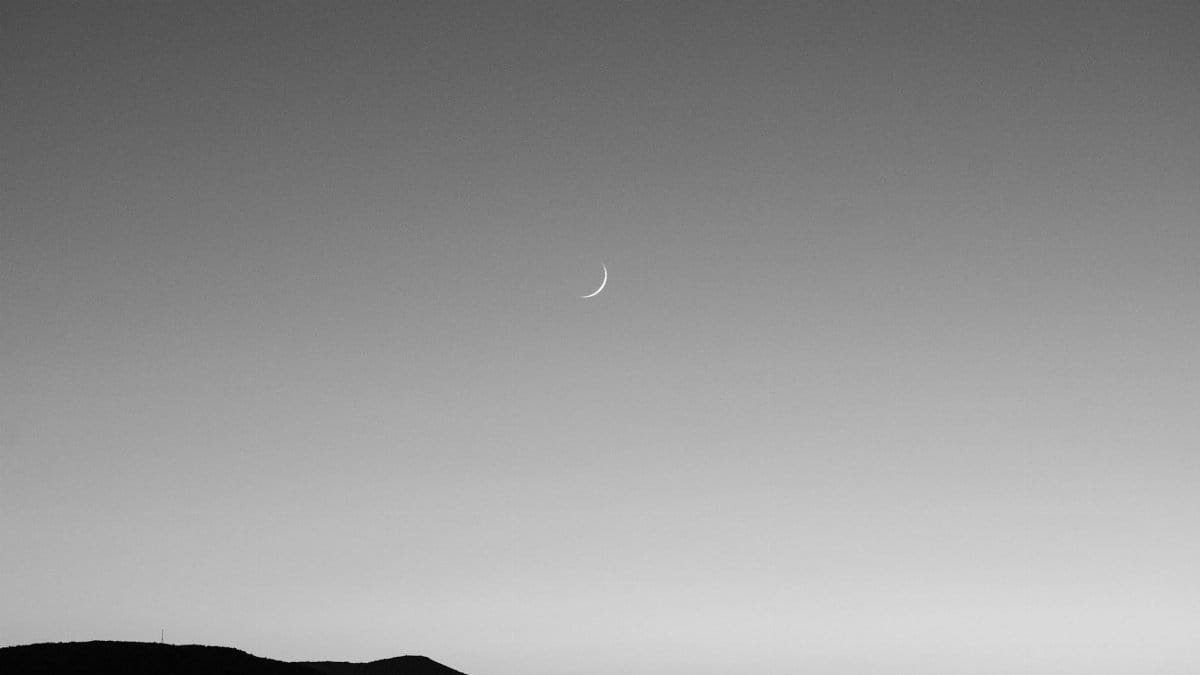 Black and white image of a crescent moon over a Podaca mountain landscape at twilight.