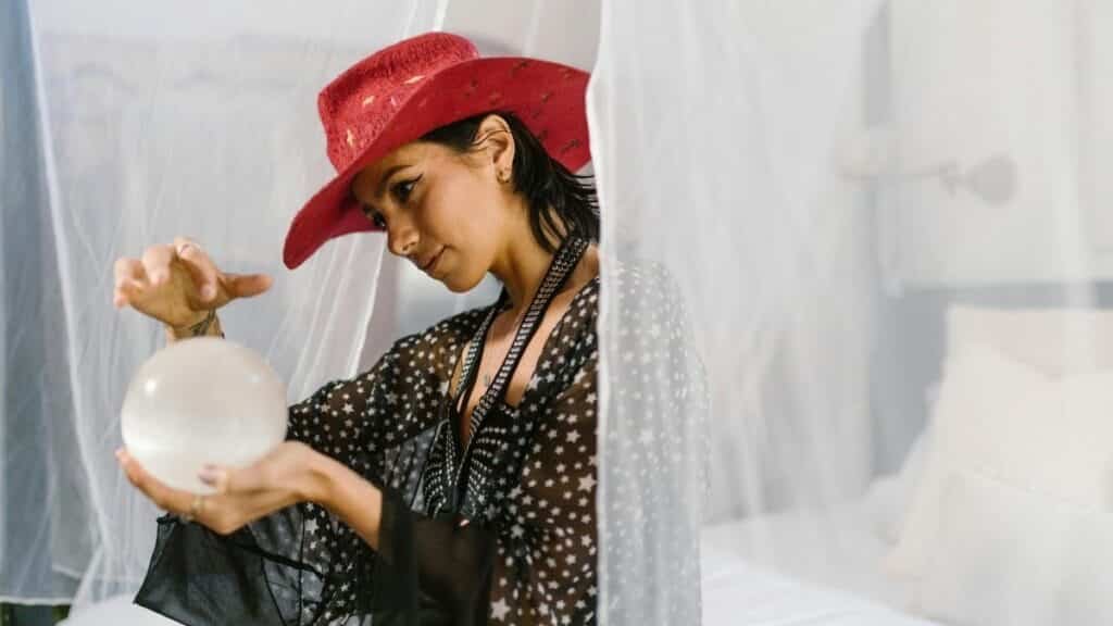A woman in a red hat examines a crystal ball in a mystical setting, evoking spiritual themes.