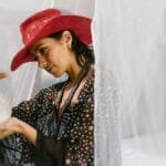 A woman in a red hat examines a crystal ball in a mystical setting, evoking spiritual themes.