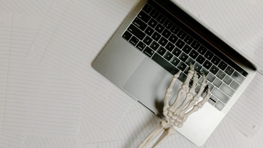 Skeleton hand on laptop keyboard overlaid on papers, symbolizing burnout.