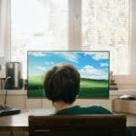 Teenager sitting indoors at a computer enjoying summer. Back view with sound system and natural lighting.