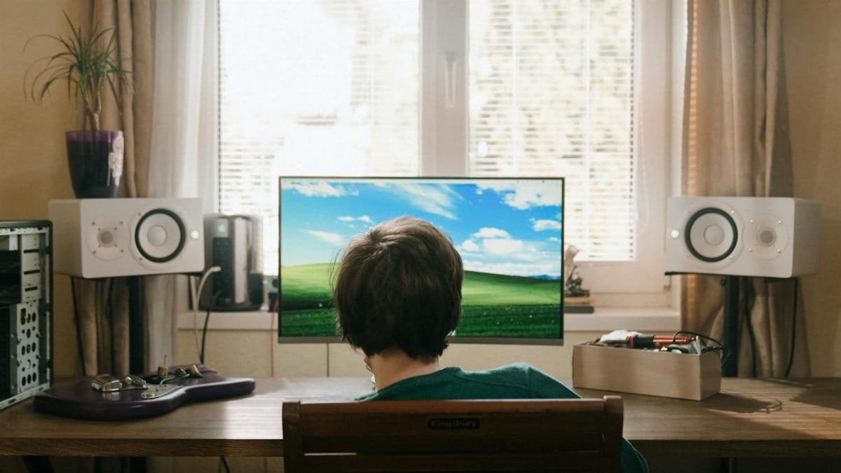 Teenager sitting indoors at a computer enjoying summer. Back view with sound system and natural lighting.