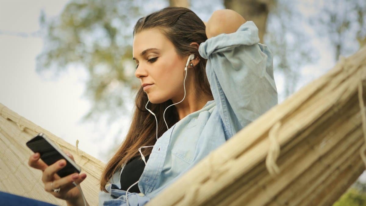 Young woman enjoying music outdoors with smartphone and earphones, embracing leisure and relaxation.