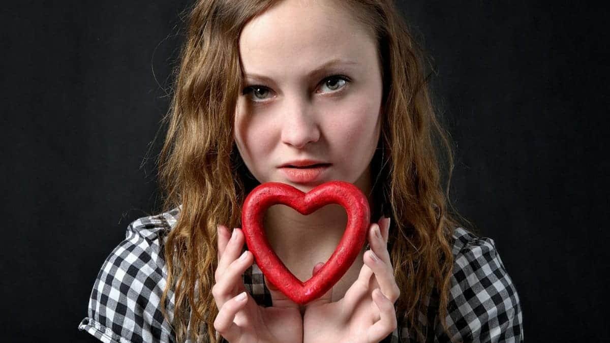 A young woman with wavy hair holding a red heart shape, symbolizing love and emotion.