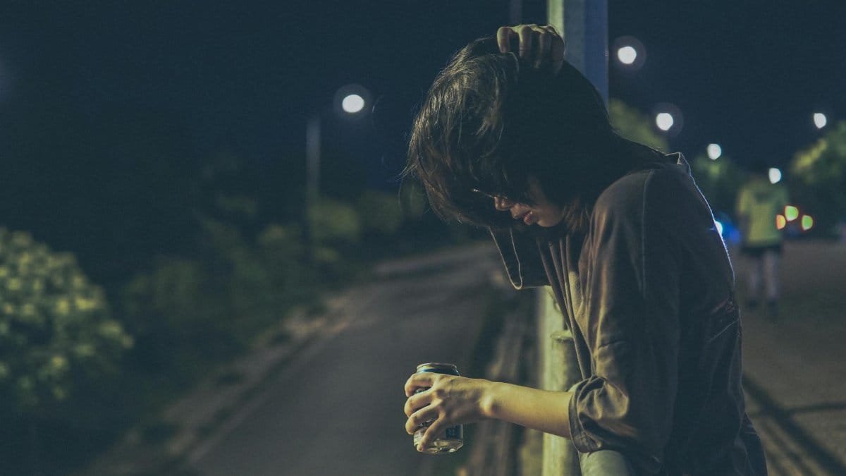 Person standing alone at night, leaning with a drink, capturing a contemplative mood.