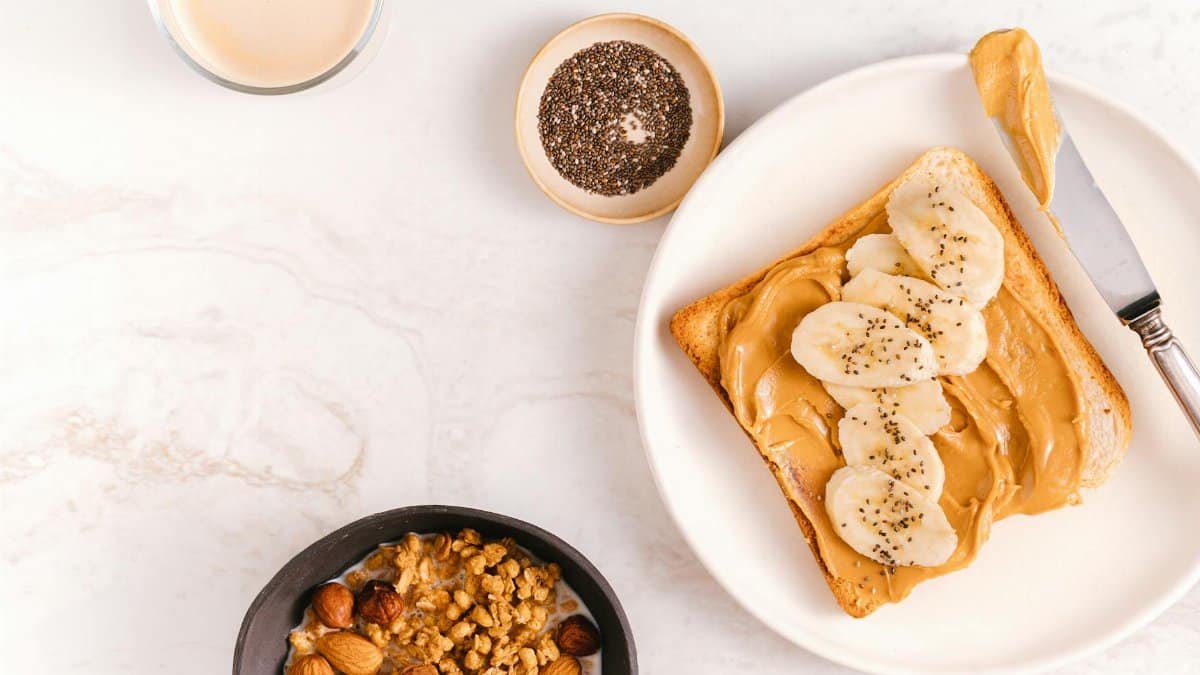 Flat lay of a nutritious breakfast featuring banana toast, chia seeds, and nuts on a marble surface.
