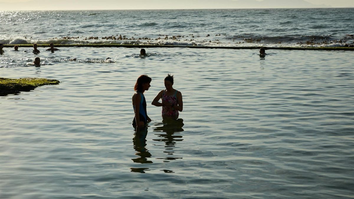 People wade through shallow waters during a picturesque beach sunset, capturing serene coastal beauty.