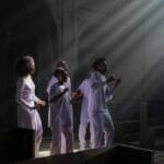 A diverse group singing in a church, illuminated by sunrays through a window.