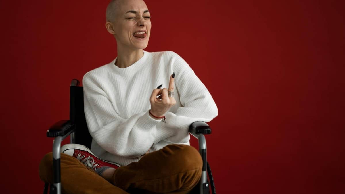 Bald woman in wheelchair expressing joy with tongue out, studio setting.