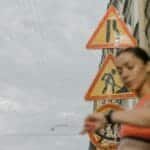 A blurred woman in sportswear checks her watch against a backdrop of urban road signs.