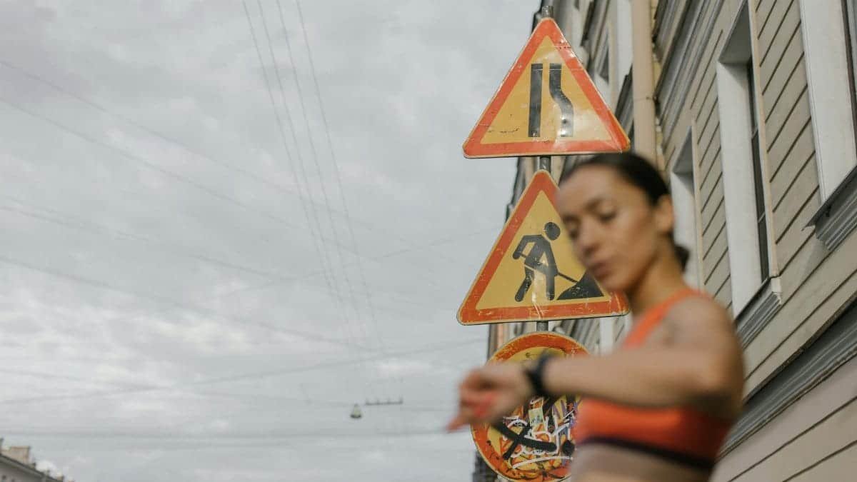 A blurred woman in sportswear checks her watch against a backdrop of urban road signs.