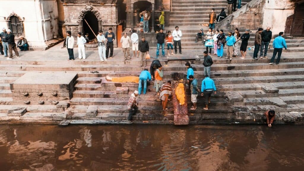 People attending a traditional funeral ceremony by a riverside in Nepal with cultural rituals.