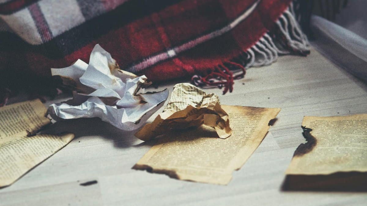 Atmospheric composition of burnt and crumpled papers with a cozy blanket in view.