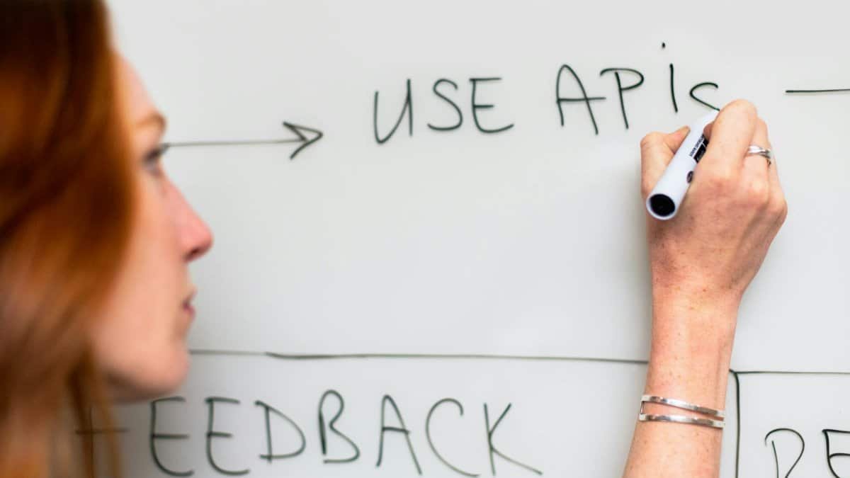 A woman writes 'Use APIs' on a whiteboard, focusing on software planning and strategy.