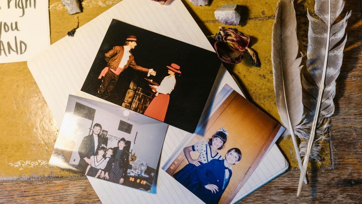 Collection of vintage family photos with feathers, crystals, and dried flowers on a notebook.