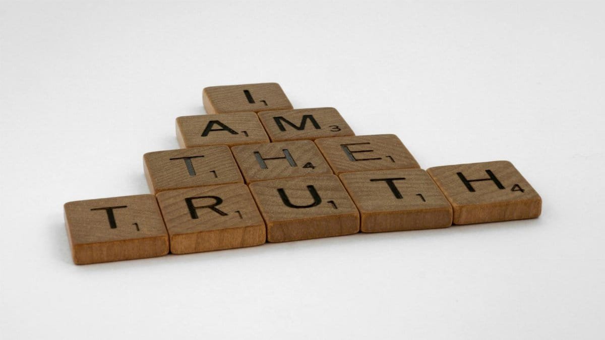 Close-up of wooden Scrabble tiles on a white background spelling 'I Am The Truth'.