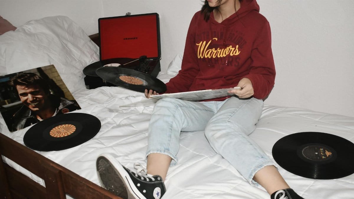 Teen girl in hoodie enjoying vinyl records in a cozy bedroom. Relaxing and vintage vibe.
