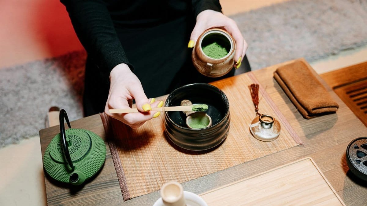 Hands preparing matcha tea in a traditional Japanese ceremony with vibrant green and earthy tones.