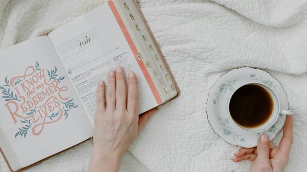 Top view of morning Bible study with coffee, featuring open Bible and feminine hands.