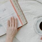 Top view of morning Bible study with coffee, featuring open Bible and feminine hands.