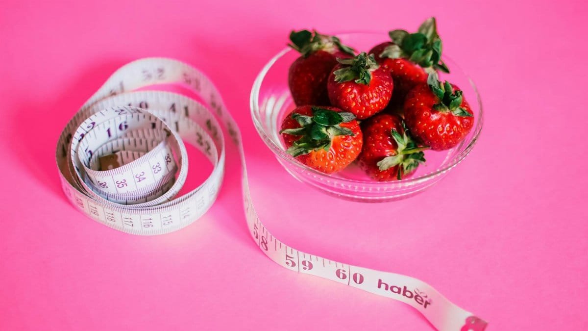 A glass bowl of fresh strawberries paired with a pink measuring tape symbolizes healthy eating.