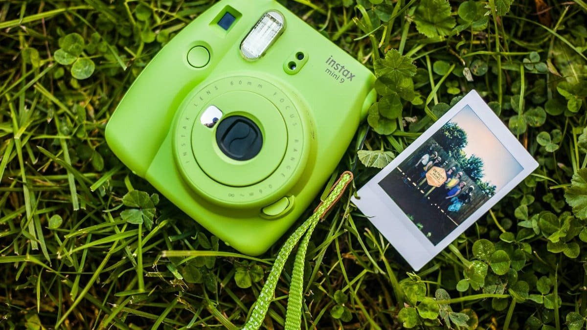 A green Instax Mini 9 camera on grass with a printed photo, highlighting casual outdoor photography.
