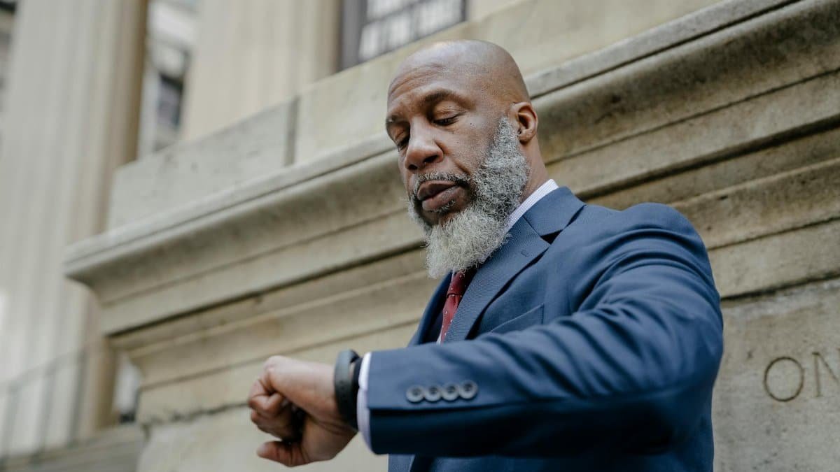 African American man in a suit checking time on a watch outside an office building.
