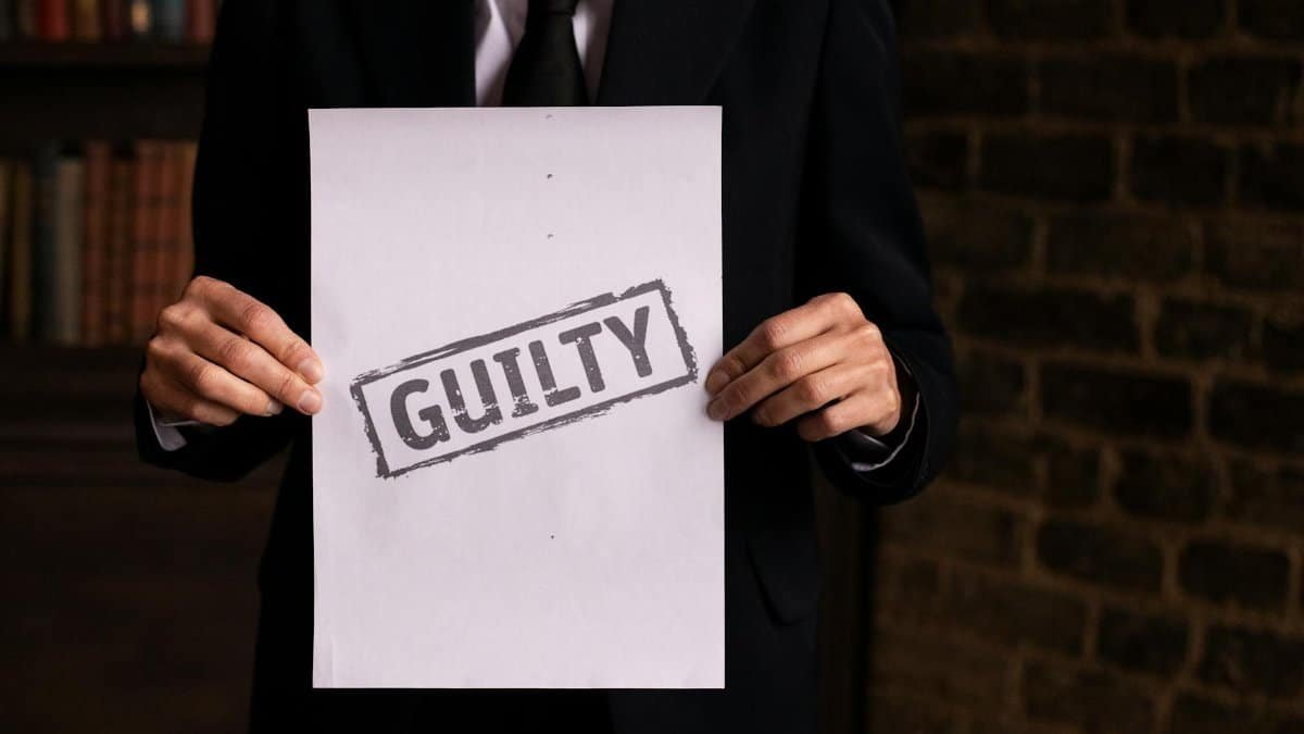 A businessman in a formal suit holding a sign with the word 'GUILTY.'