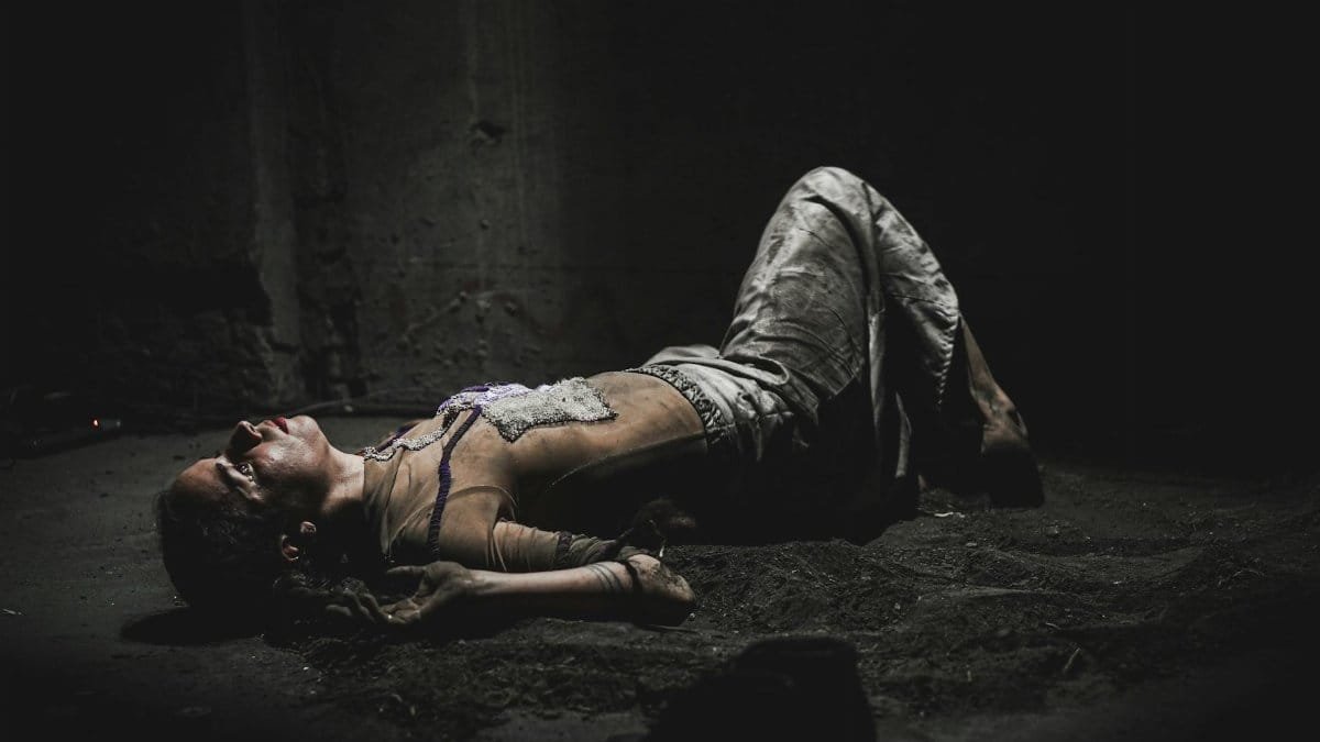 A woman lies on a dark floor, evoking themes of despair and pain.