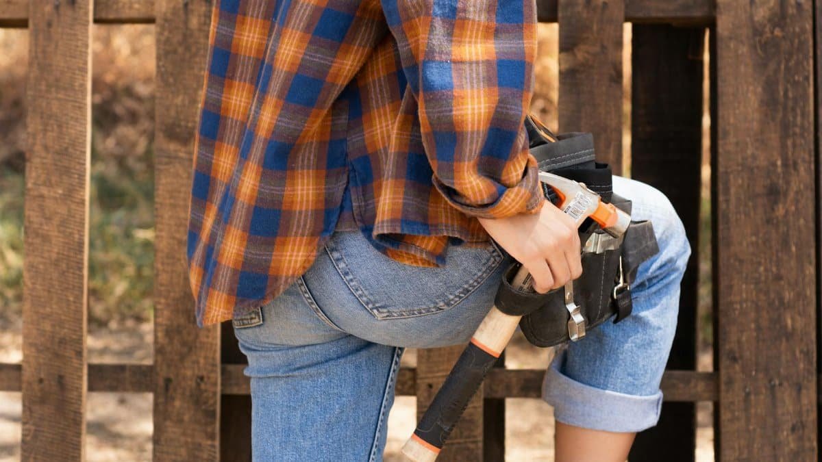 Female carpenter holding tool belt against wooden backdrop, showcasing empowerment and skill.