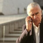 Serious senior businessman using a smartphone outdoors, conveying a professional and pensive mood.