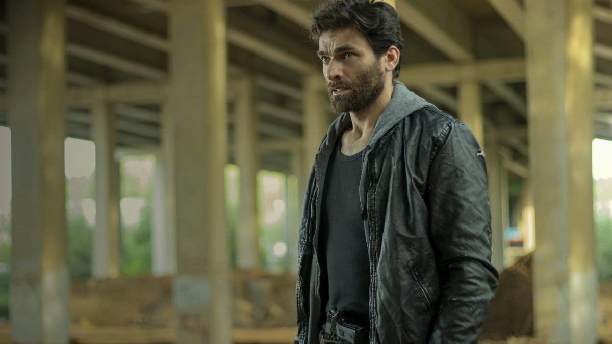 A man in a leather jacket stands under a bridge, embodying a gritty urban aesthetic.