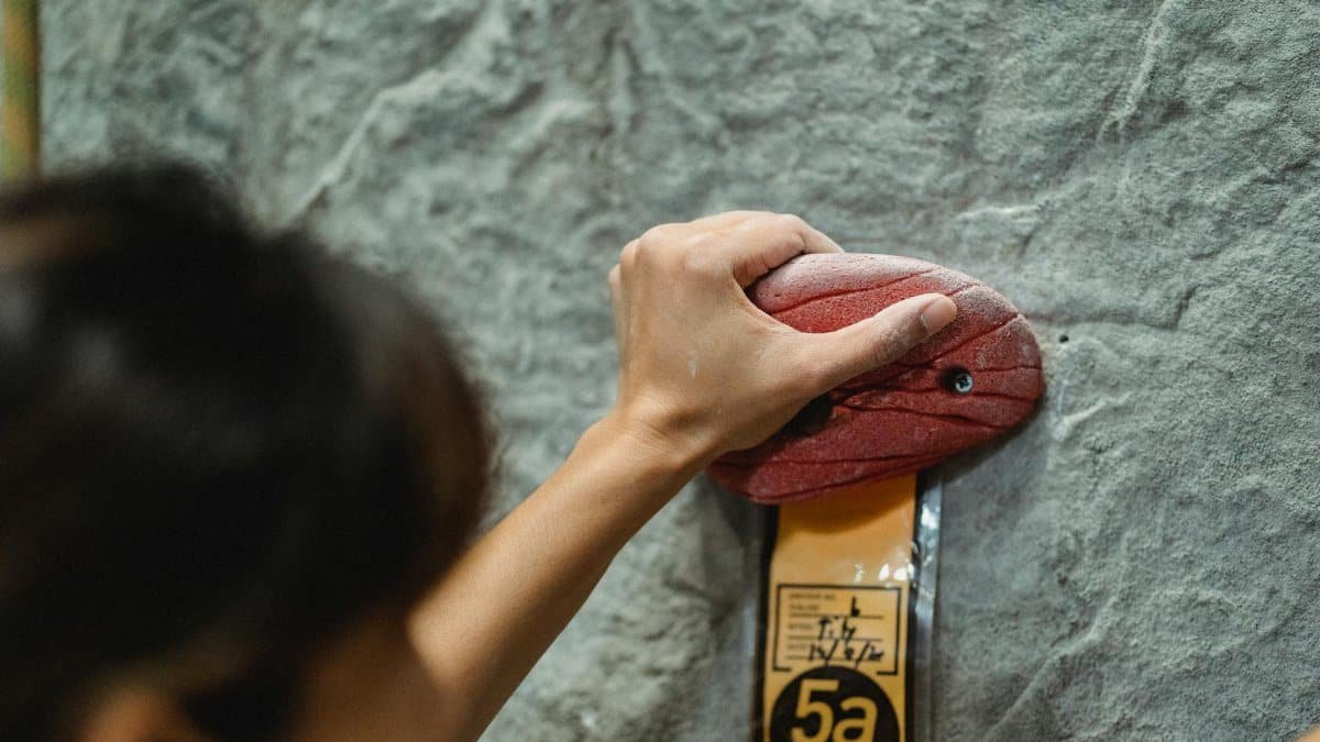 Close-up of a woman's hand gripping an indoor climbing wall hold, showcasing focus and strength.
