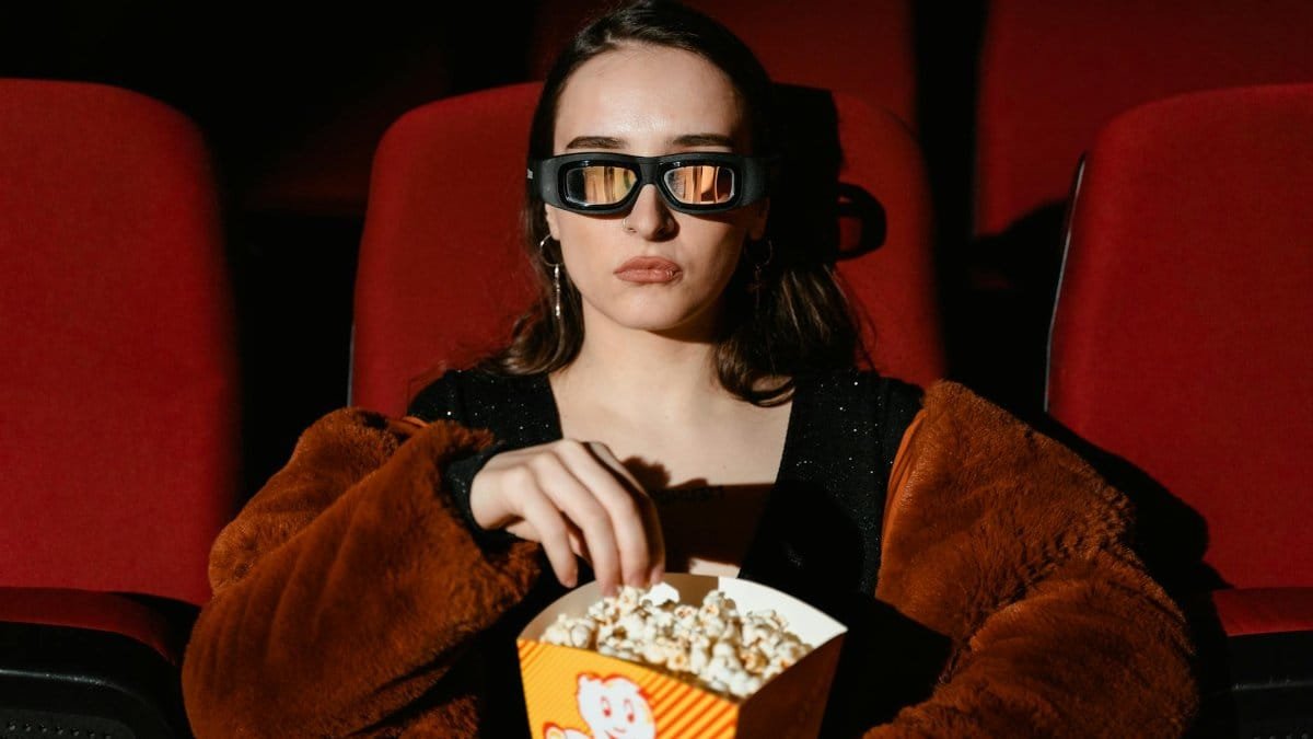 A woman in a fur coat enjoying popcorn while watching a 3D movie in a cinema.