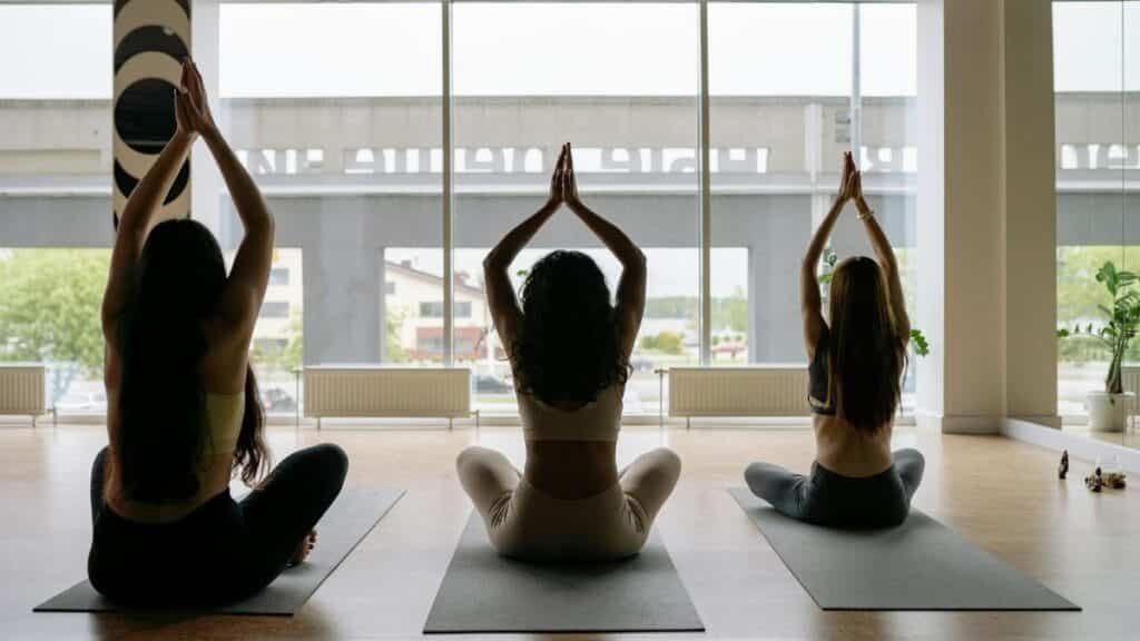 Three women performing yoga poses on mats in a sunlit studio. The scene exudes tranquility and focus.