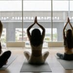 Three women performing yoga poses on mats in a sunlit studio. The scene exudes tranquility and focus.