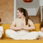 A mother and her children practicing mindfulness meditation on a sofa indoors.