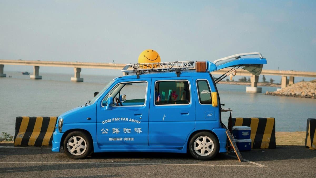 A bright blue van with a smiley face, parked by a bridge on a sunny day.