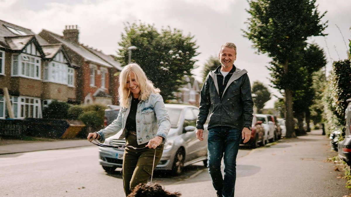 A joyous senior couple walking their dog on a sunny suburban street, enjoying the day.
