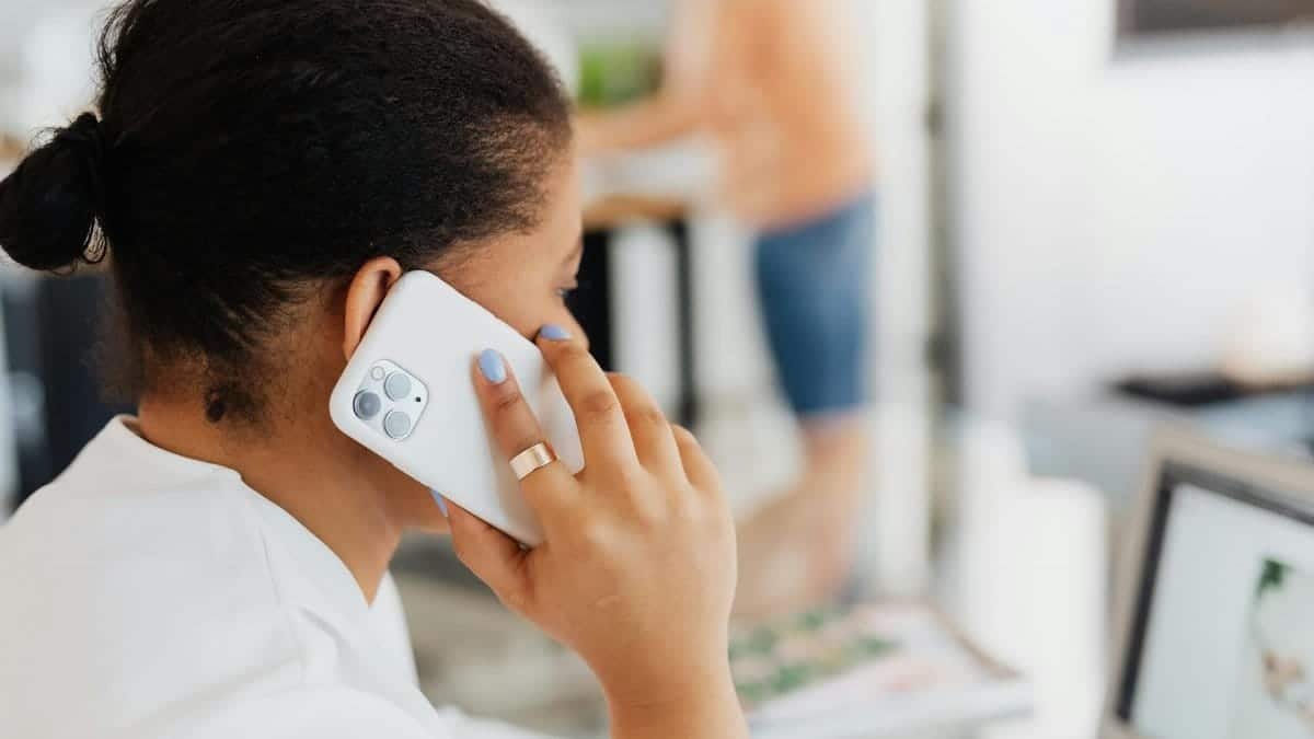 Adult woman making a call in an office, using a modern smartphone and laptop, conveying communication.
