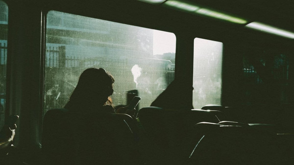 Silhouette of a person using a phone on a train journey, sunlight streaming in.