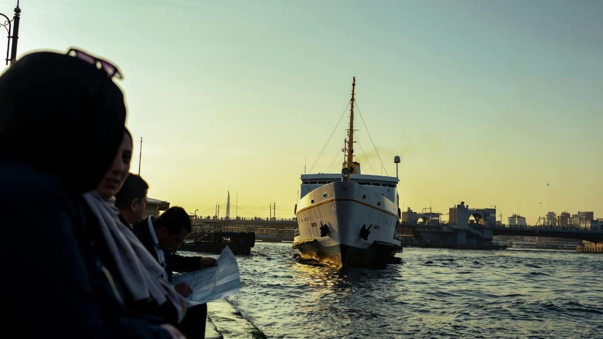 Ferry approaching harbor with people watching at sunset, offering serene maritime vibes.