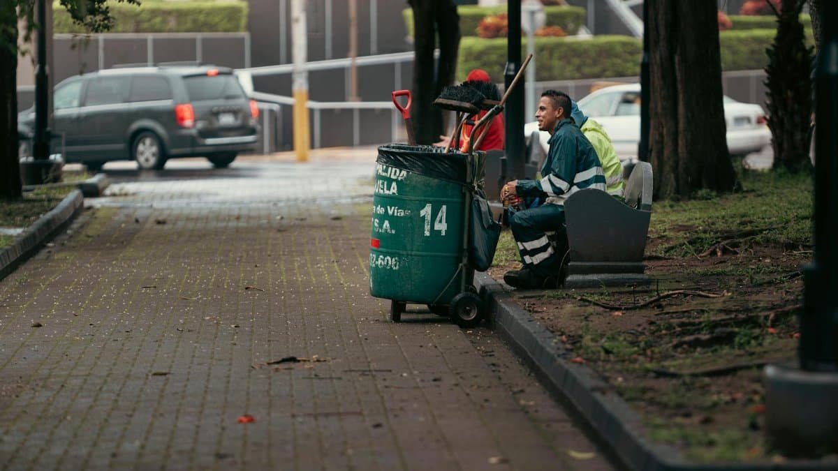 Street cleaner resting with equipment in city park, Alajuela, Costa Rica.
