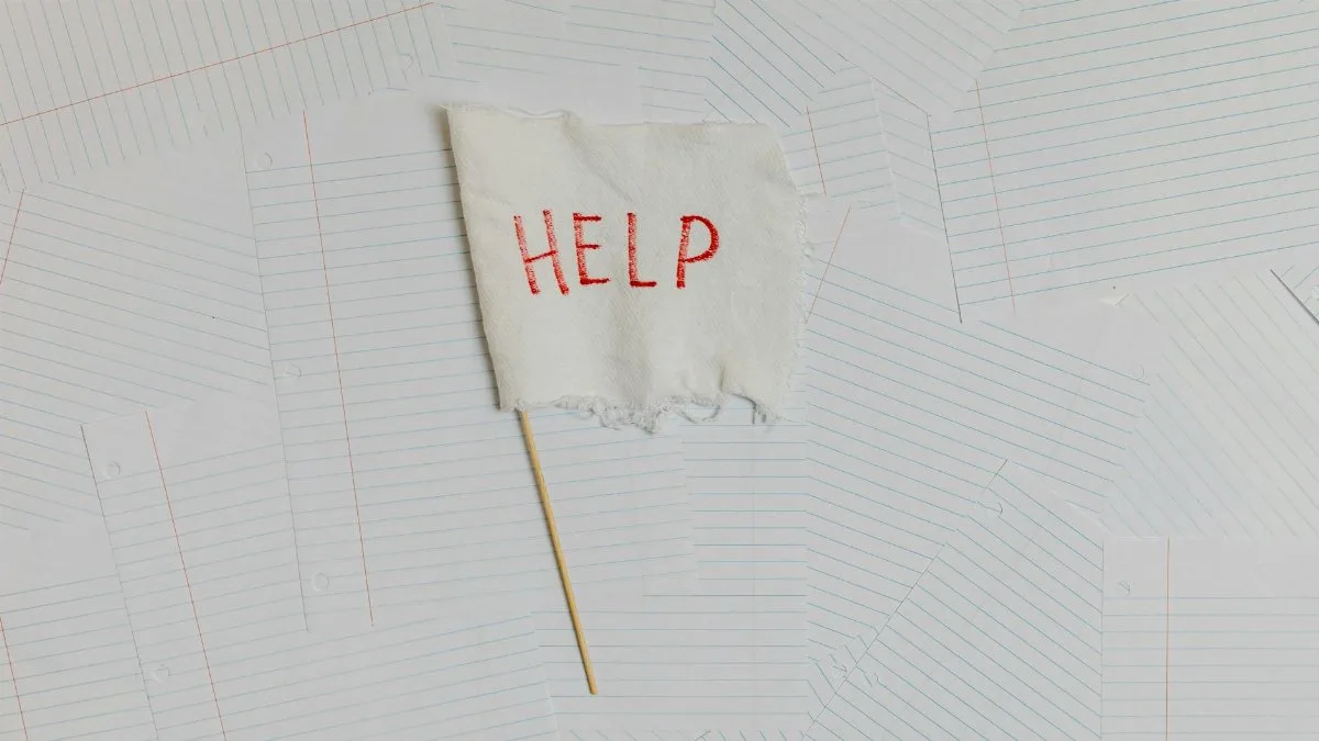 A fabric flag with 'HELP' on a scattered notepaper background, symbolizing distress or overwhelm.