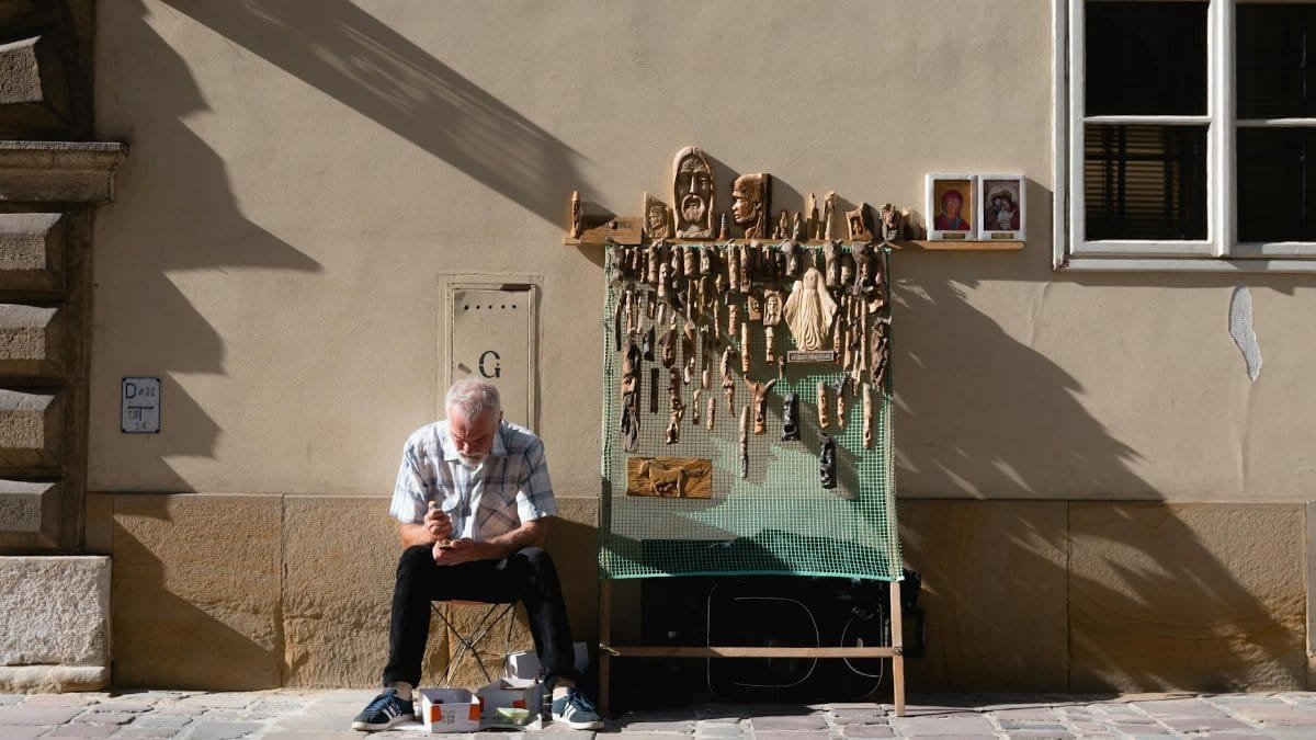 An elderly man crafting wooden sculptures on a street in Kraków, Poland, showcasing traditional arts and crafts.
