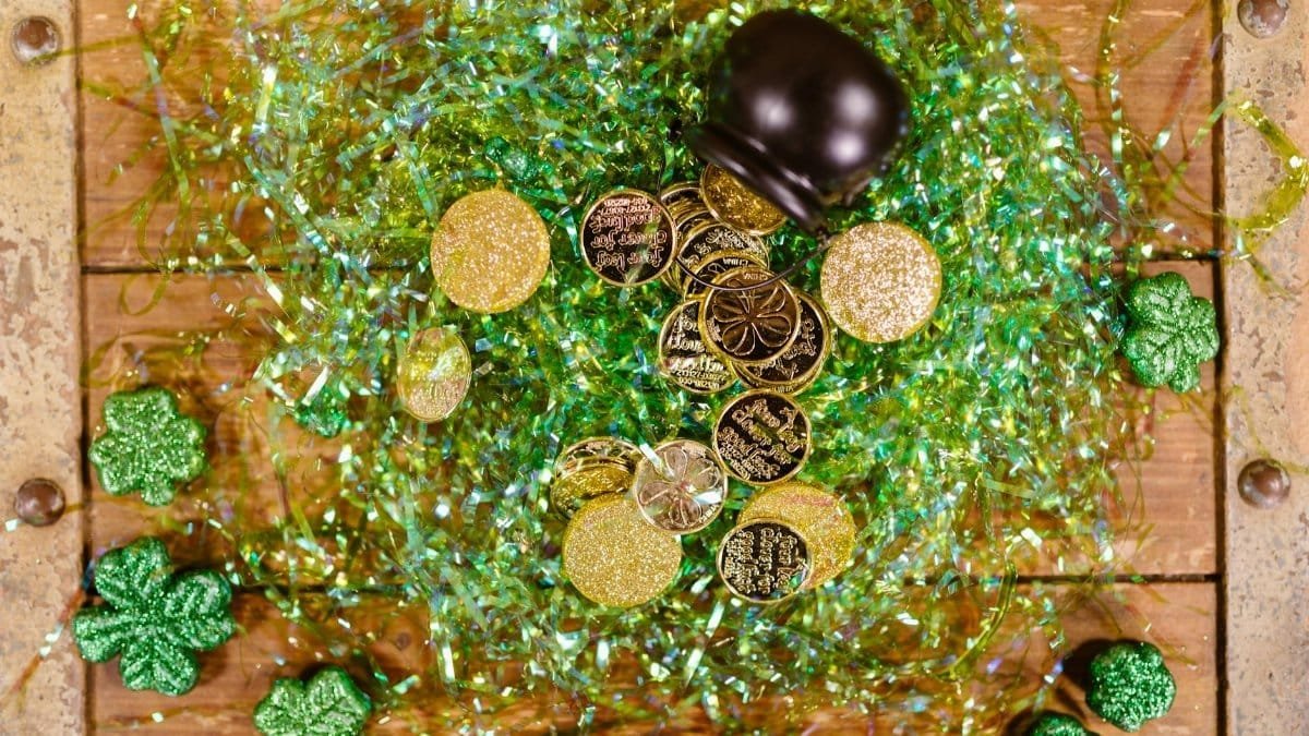 Overhead view of gold coins and shamrocks celebrating St. Patrick's Day with festive green tinsel.