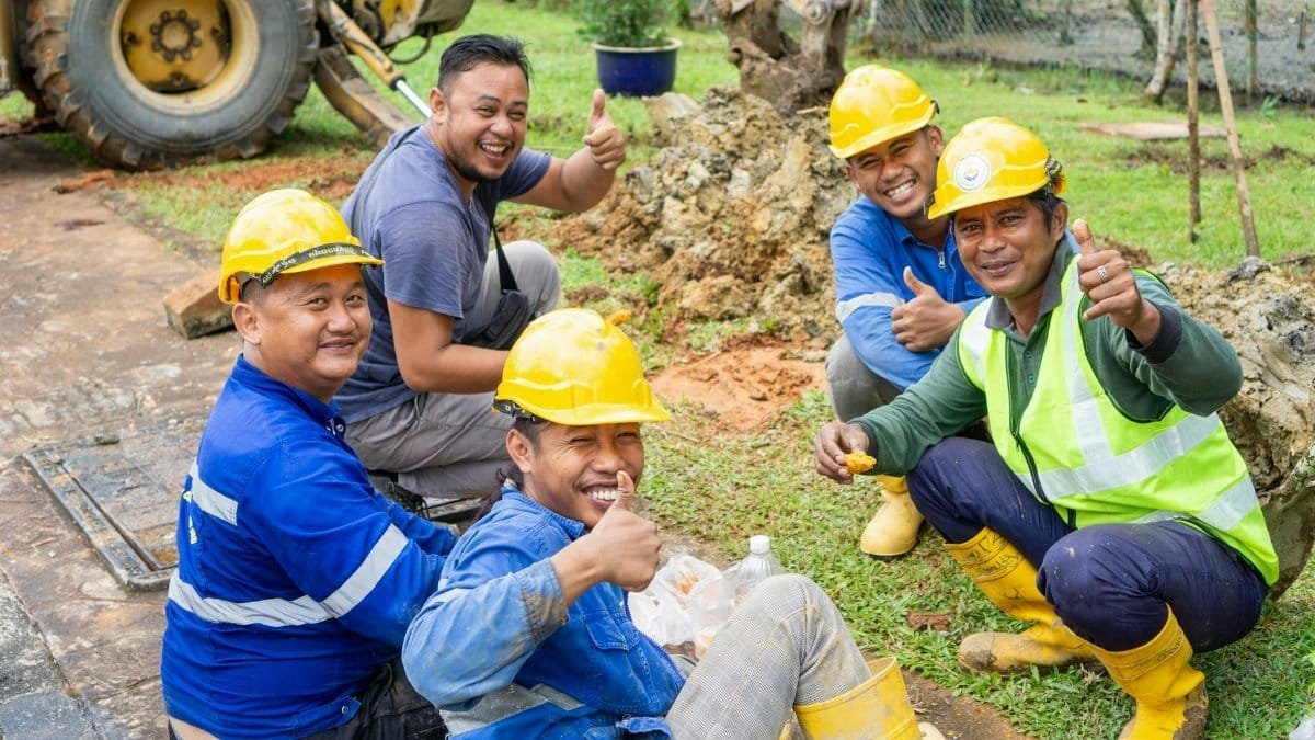 Group of smiling construction workers in safety gear taking a break outside.